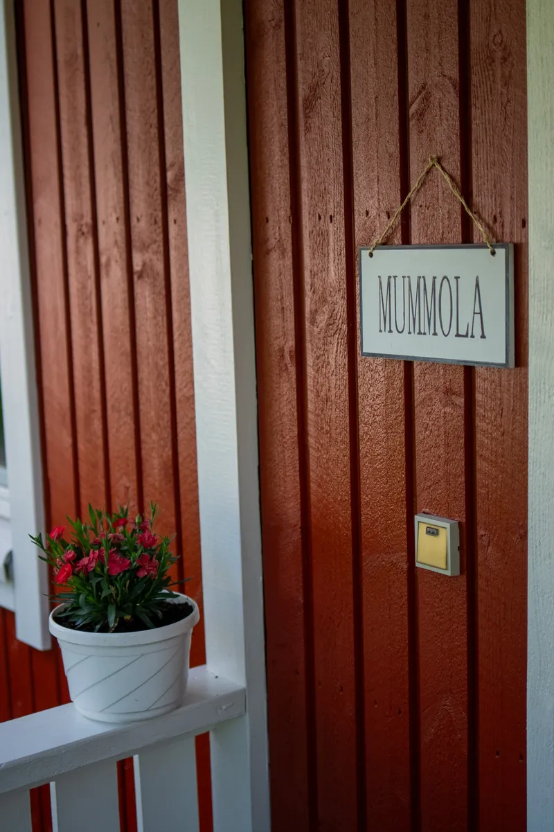 Mummola-kyltti punaisen puutalon seinällä ja kukkia kaiteella